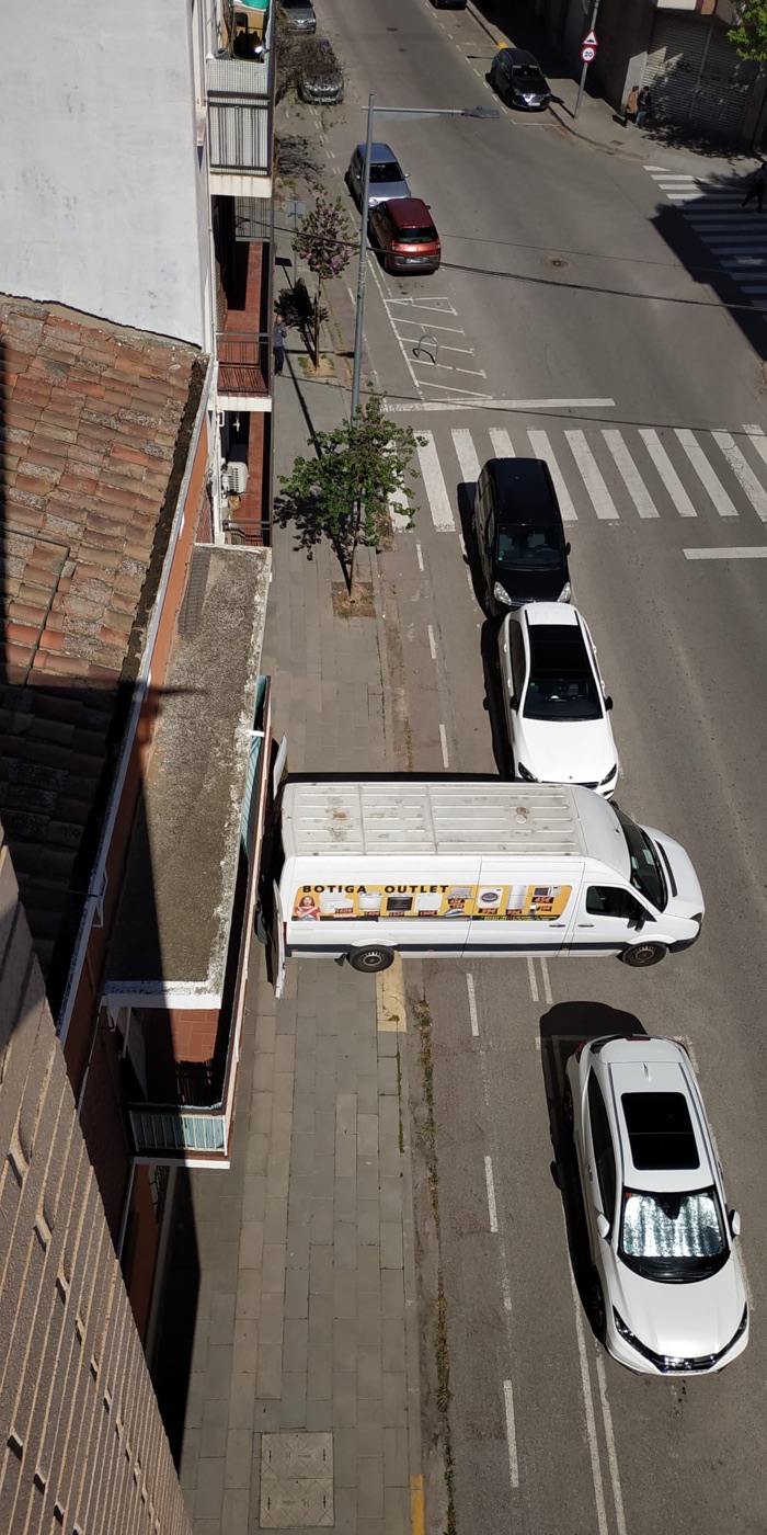 Una furgoneta i diversos cotxes ocupant el carril bici i la vorera d'un carrer de Lleida, vist des de dalt.